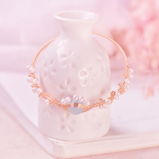 Gold and pearl bracelet on a white ceramic vase with a blurred floral background