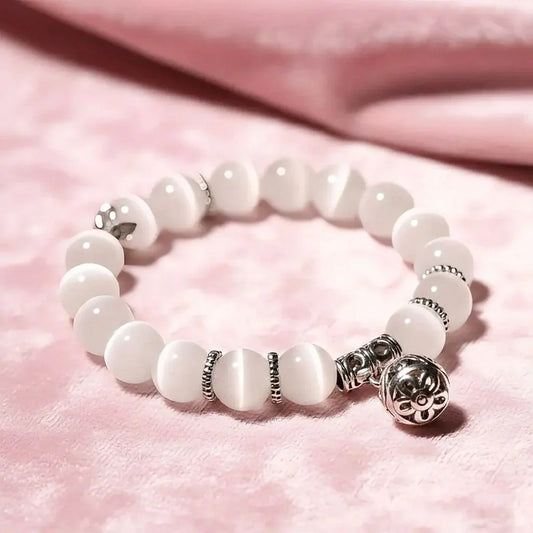 White beaded bracelet with silver charms on a pink fabric background