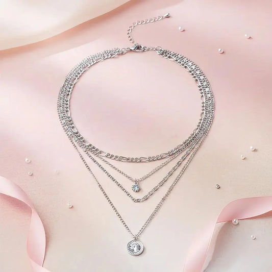 Multiple silver necklaces with pendants on a soft pink fabric background