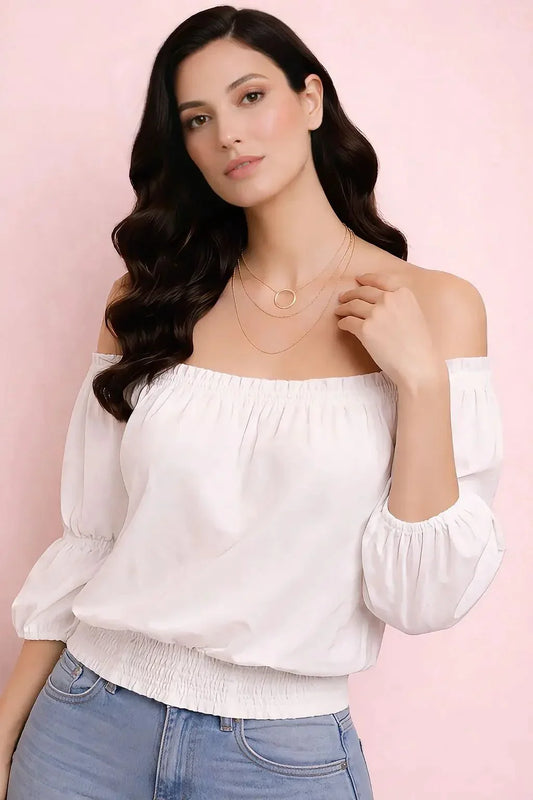 Woman wearing a white off-shoulder top and blue jeans against a pink background