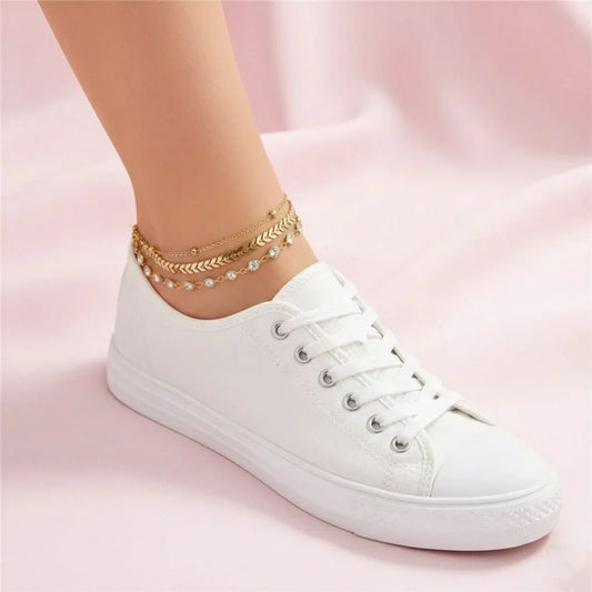 White sneaker worn with gold anklets on a pink background