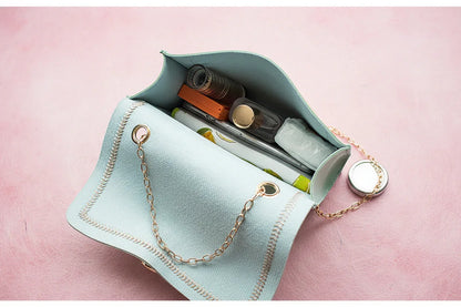 Light blue clutch bag with gold chain strap containing a phone, bottle, and other items on a light gray background