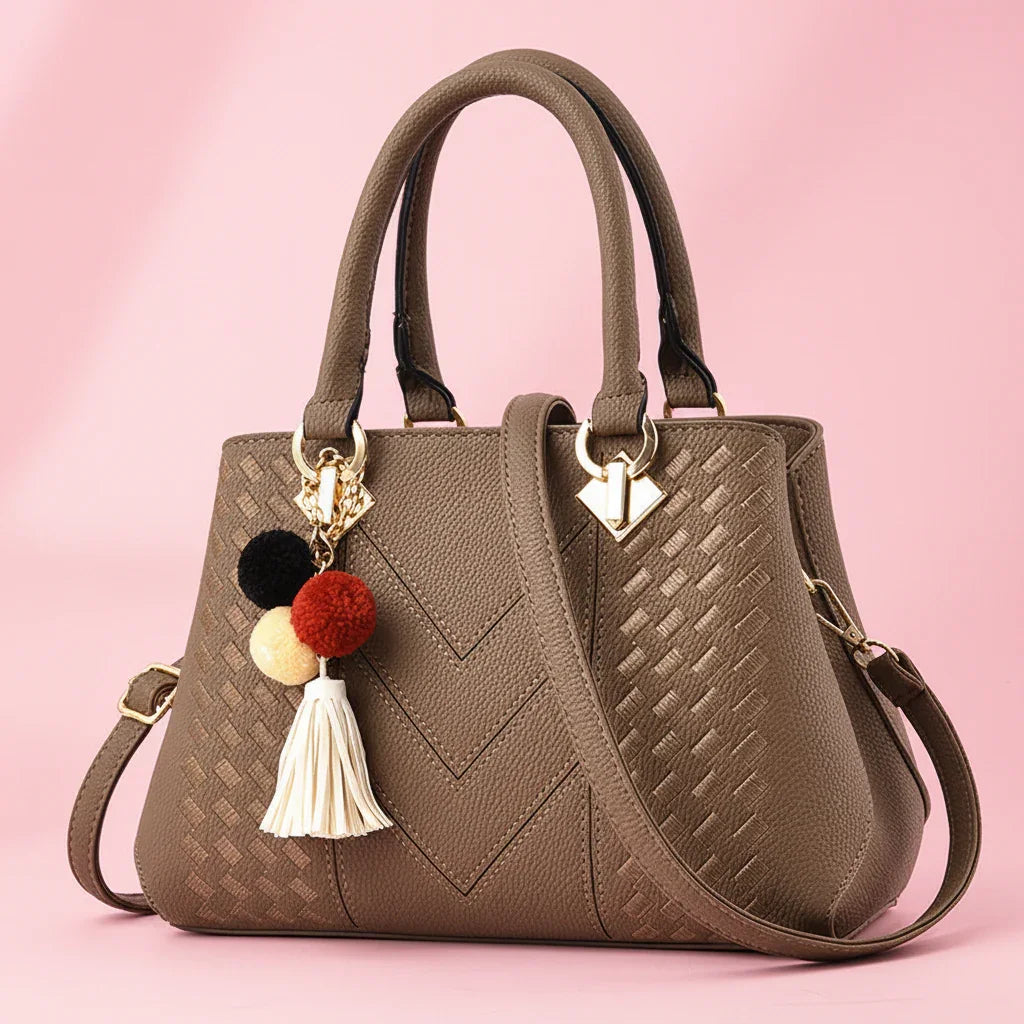 Brown handbag with decorative pom-pom keychain on a white background