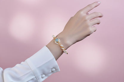 Hand wearing a gold bracelet with a blue gemstone against a dark background