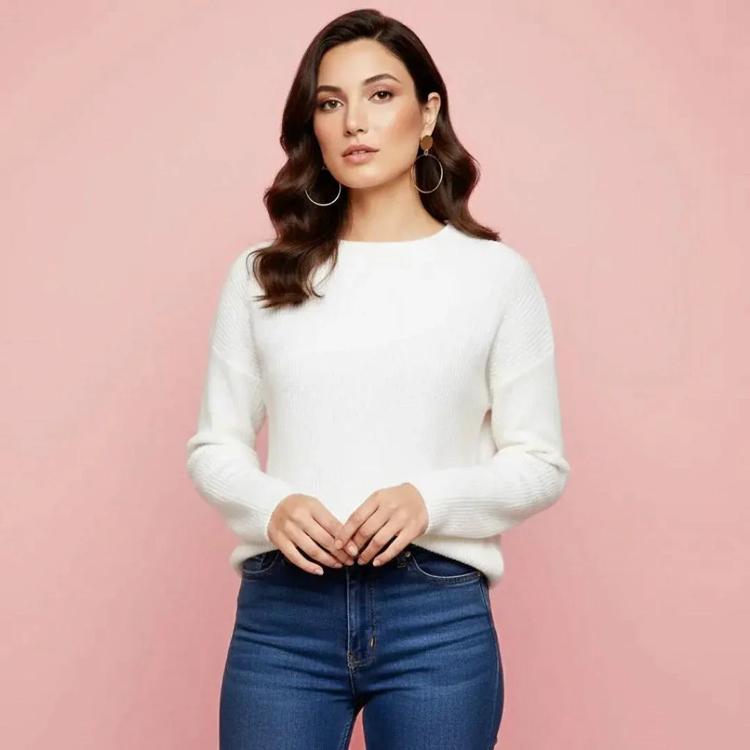 Woman wearing a white sweater and blue jeans against a pink background