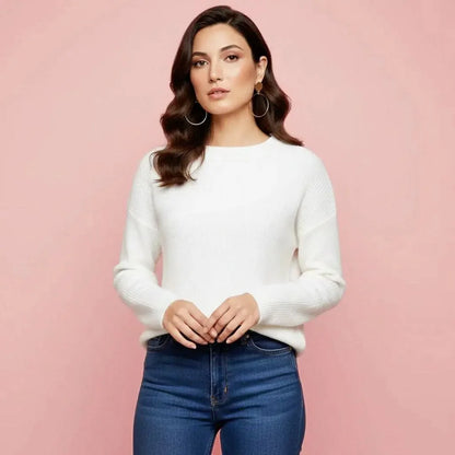 Woman wearing a white sweater and blue jeans against a pink background