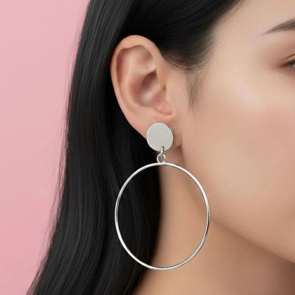 Silver hoop earrings worn by a person with a pink background