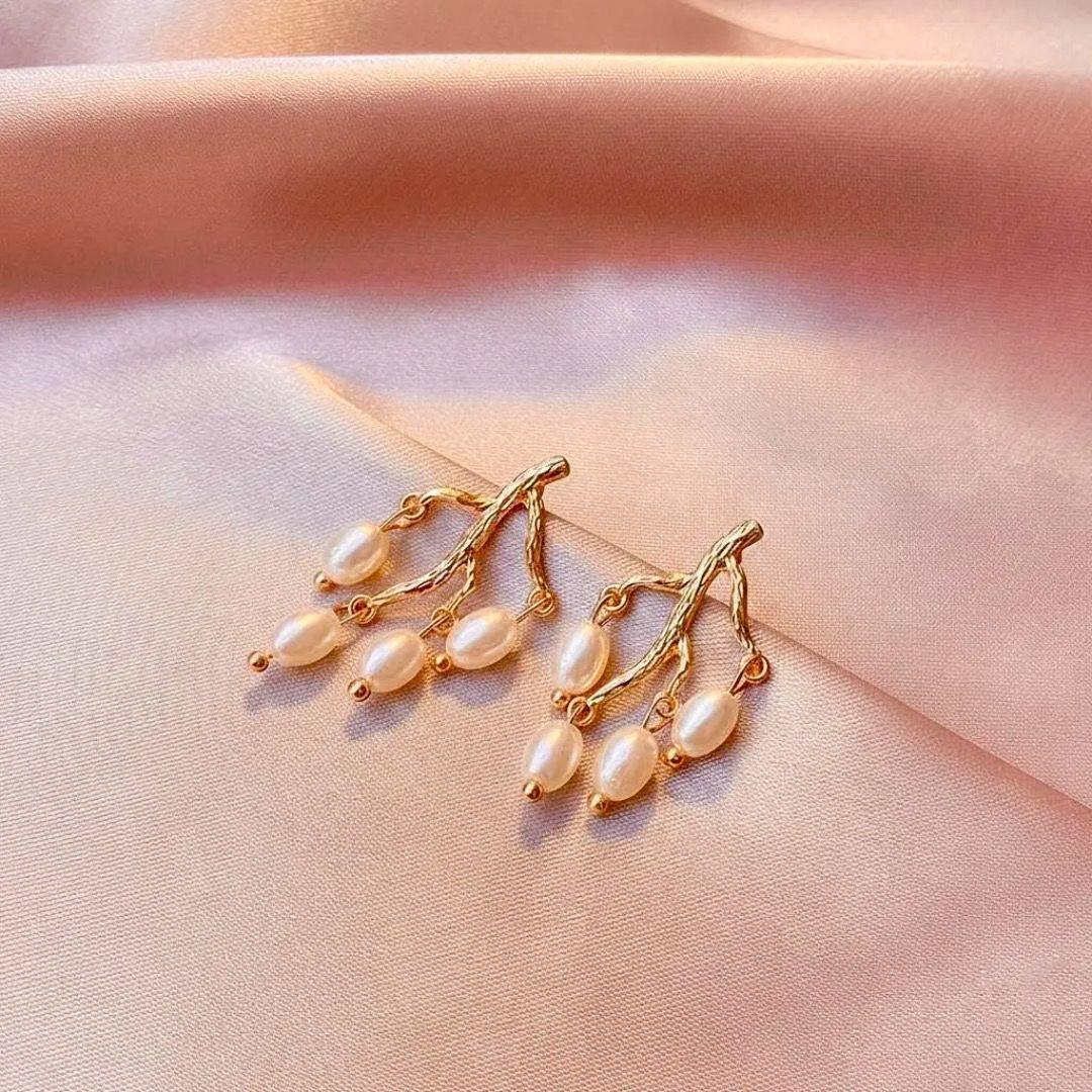 Gold earrings with pearls on a soft pink fabric background