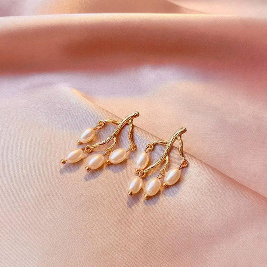 Gold earrings with pearls on a soft pink fabric background
