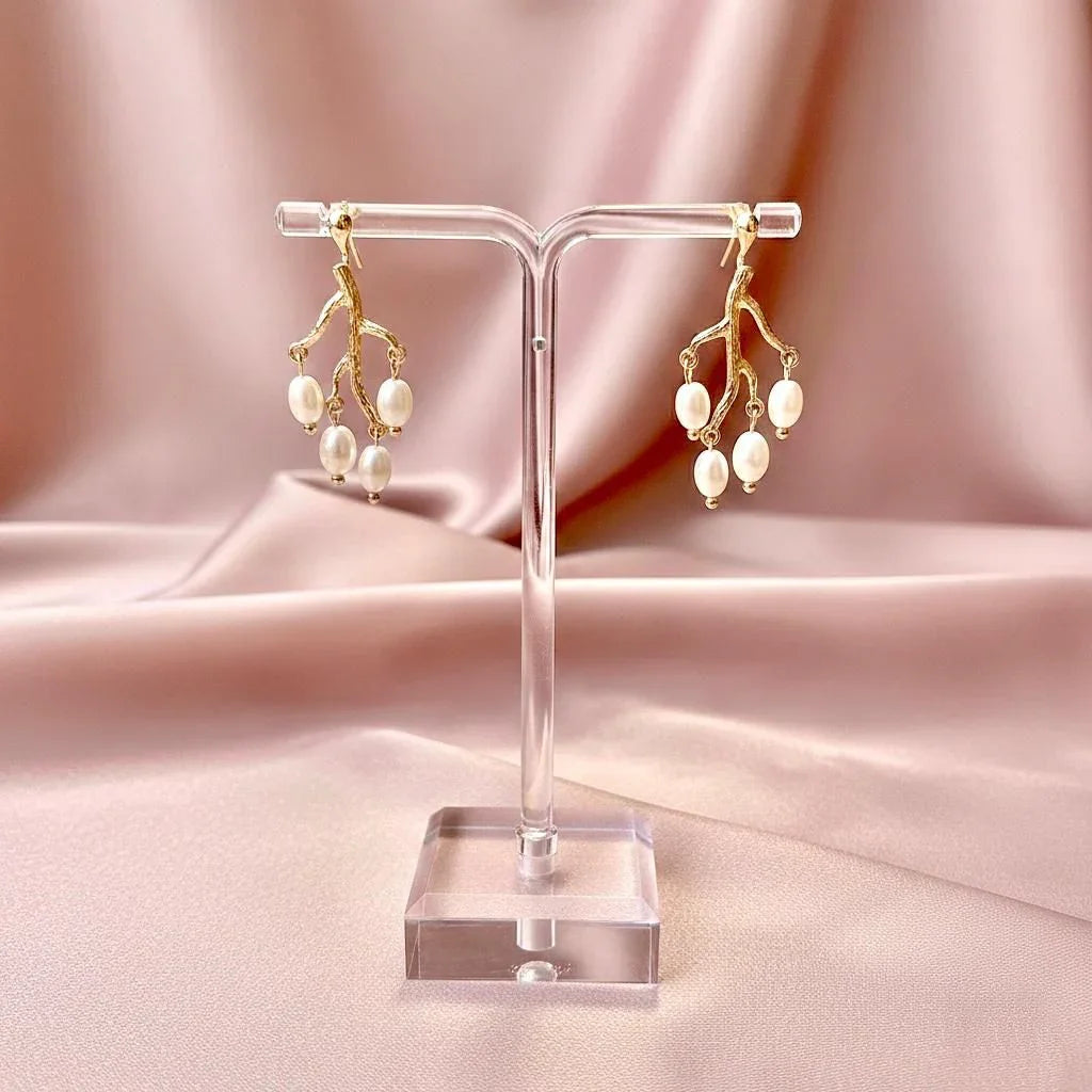 Gold and pearl earrings on a clear stand against a pink fabric background