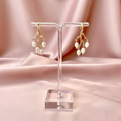Gold and pearl earrings on a clear stand against a pink fabric background