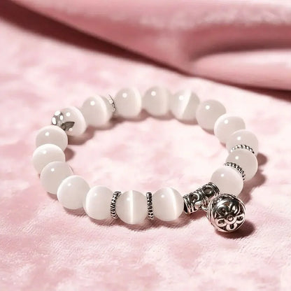 White beaded bracelet with silver charms on a pink fabric background