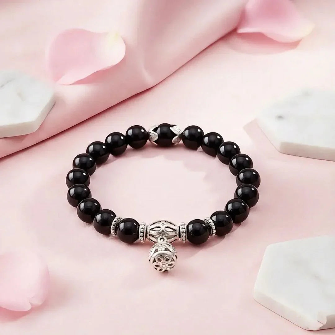 Black beaded bracelet with a silver charm on a pink fabric background