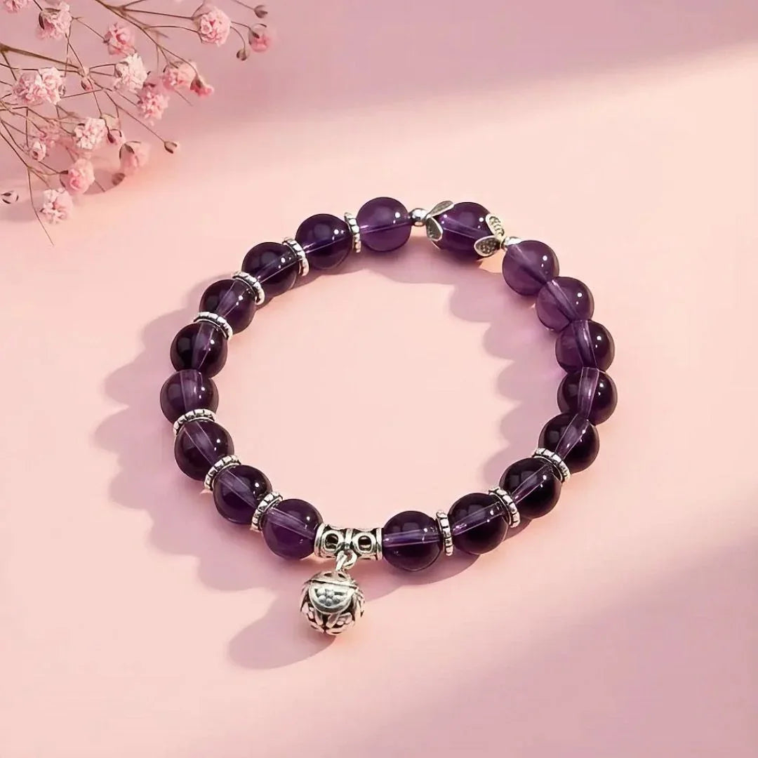 Purple beaded bracelet with a silver charm on a pink background