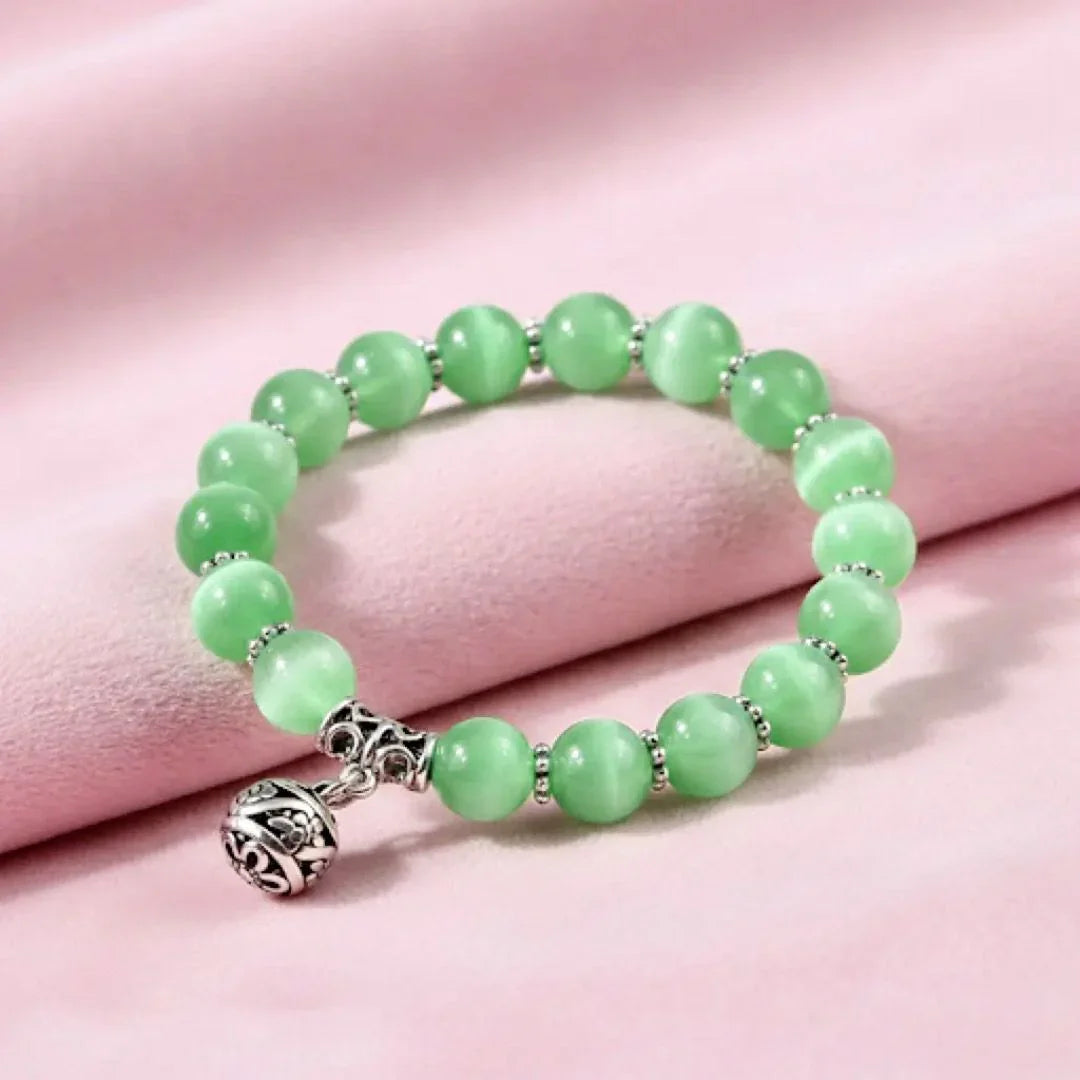 Green beaded bracelet with a silver charm on a pink fabric background