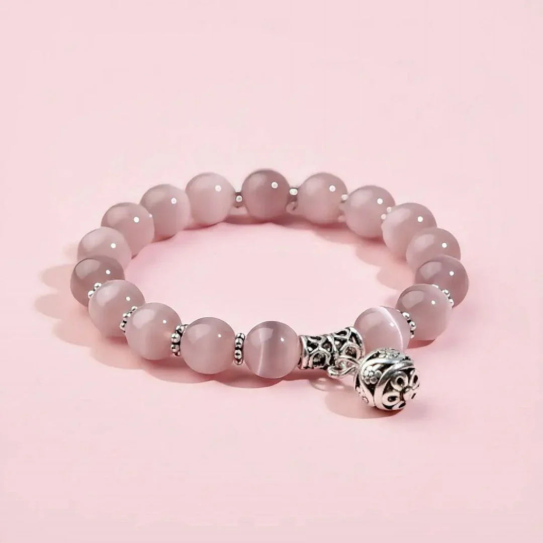 Pink beaded bracelet with a silver charm on a pink background