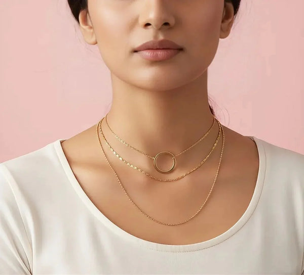 Woman wearing gold necklaces against a pink background