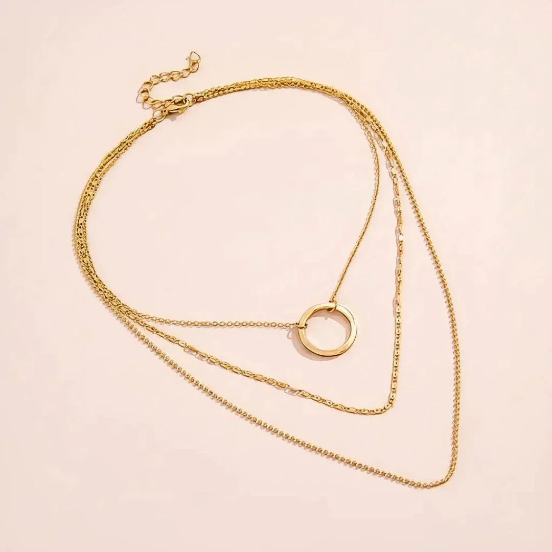 Gold necklace with a circular pendant on a light pink background