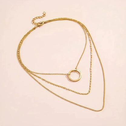 Gold necklace with a circular pendant on a light pink background