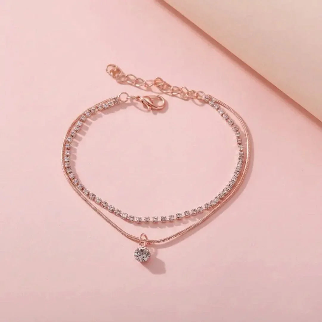 Rose gold bracelet with clear stones on a pink background