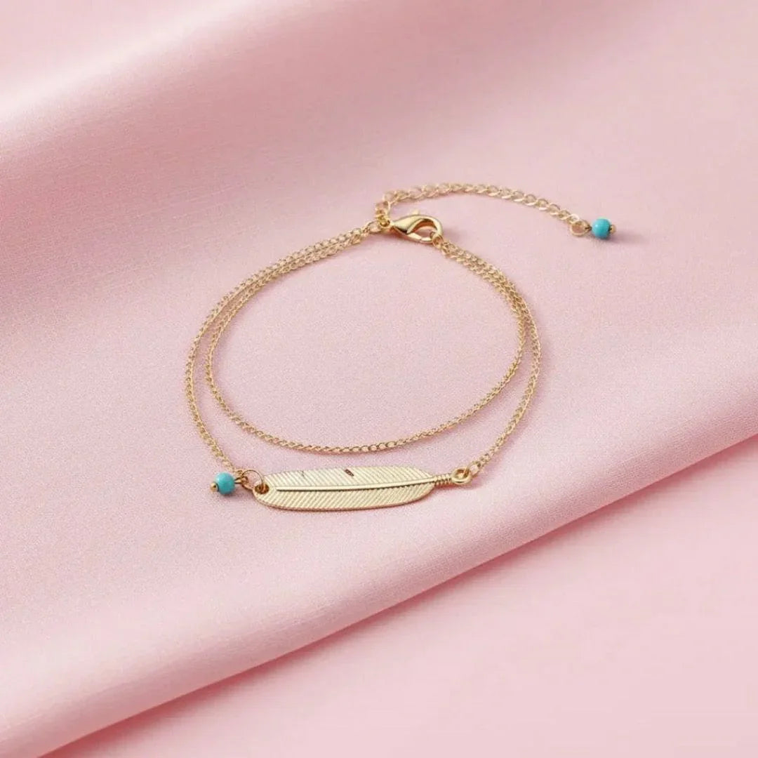 Gold bracelet with feather design on a pink fabric background