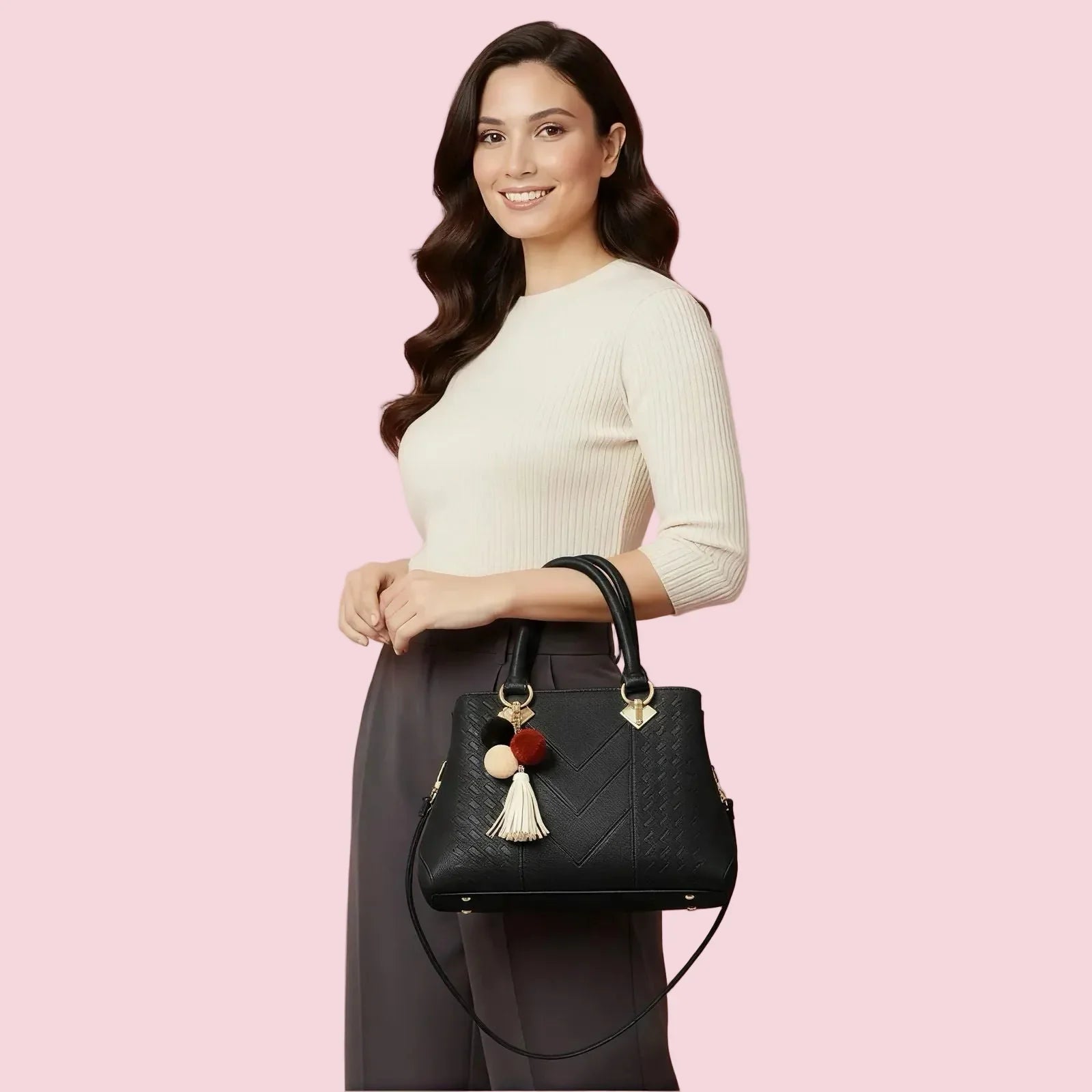 Woman holding a black handbag with decorative pom-poms against a pink background