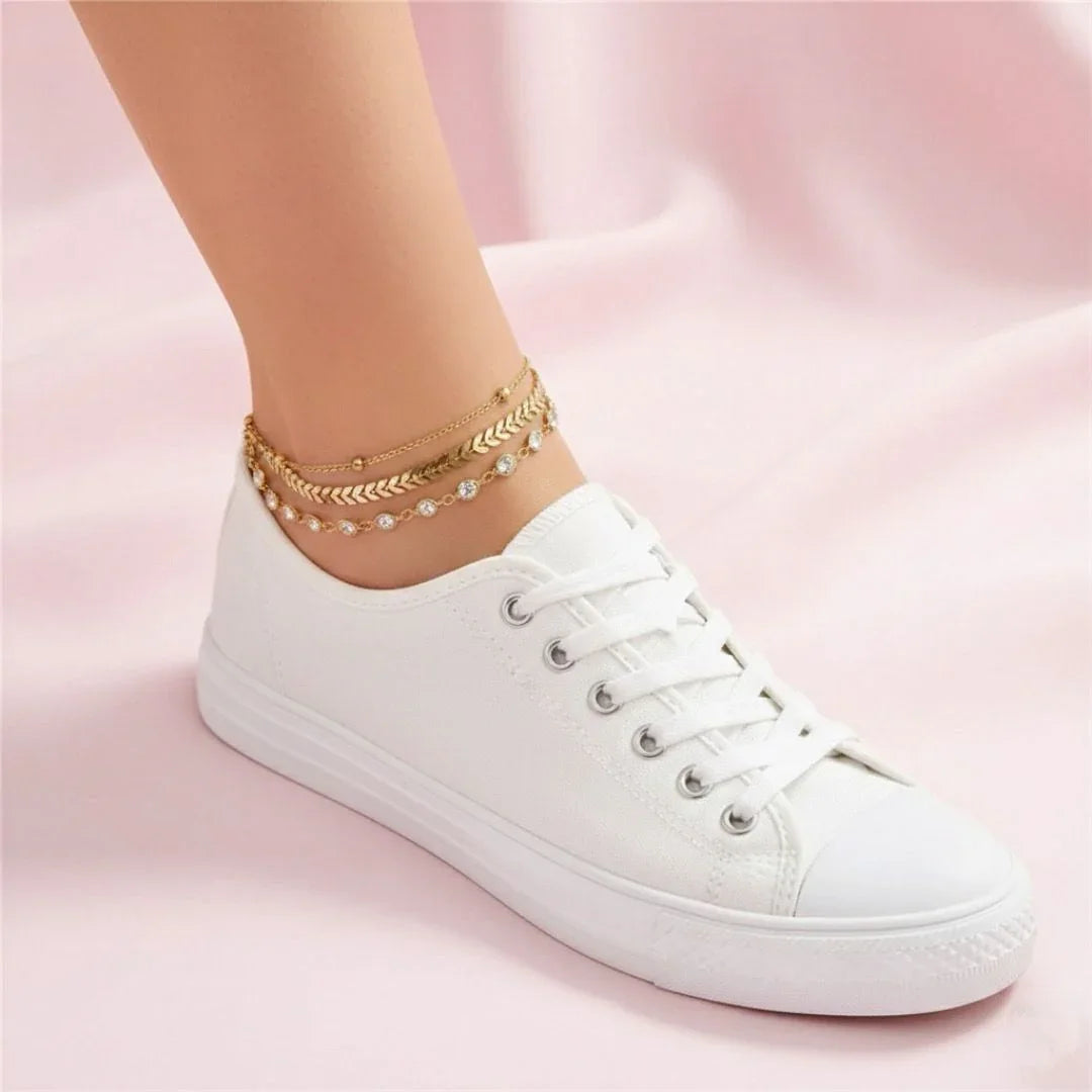White sneaker worn with gold anklets on a pink background