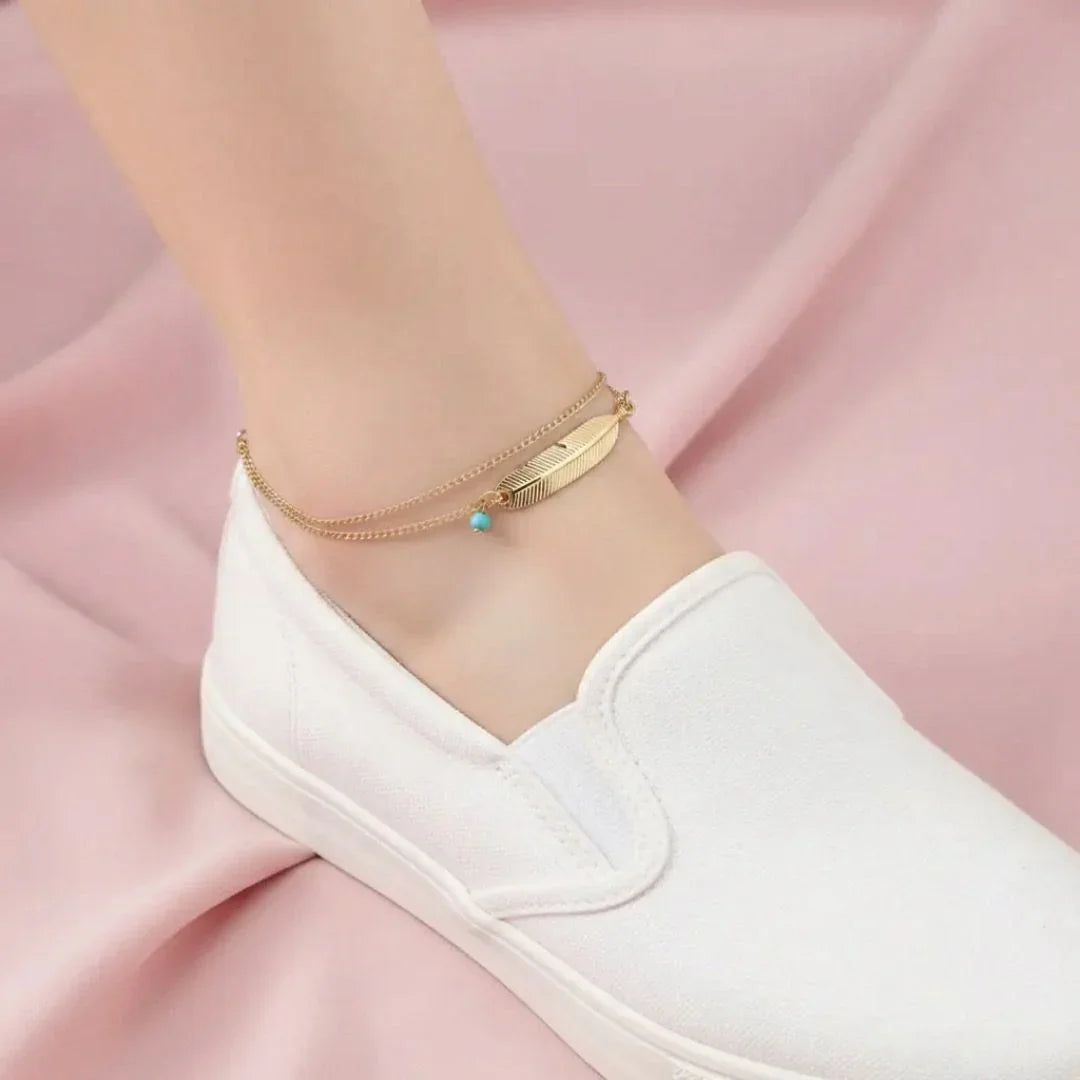 Gold anklets on a person's ankle with a pink fabric background