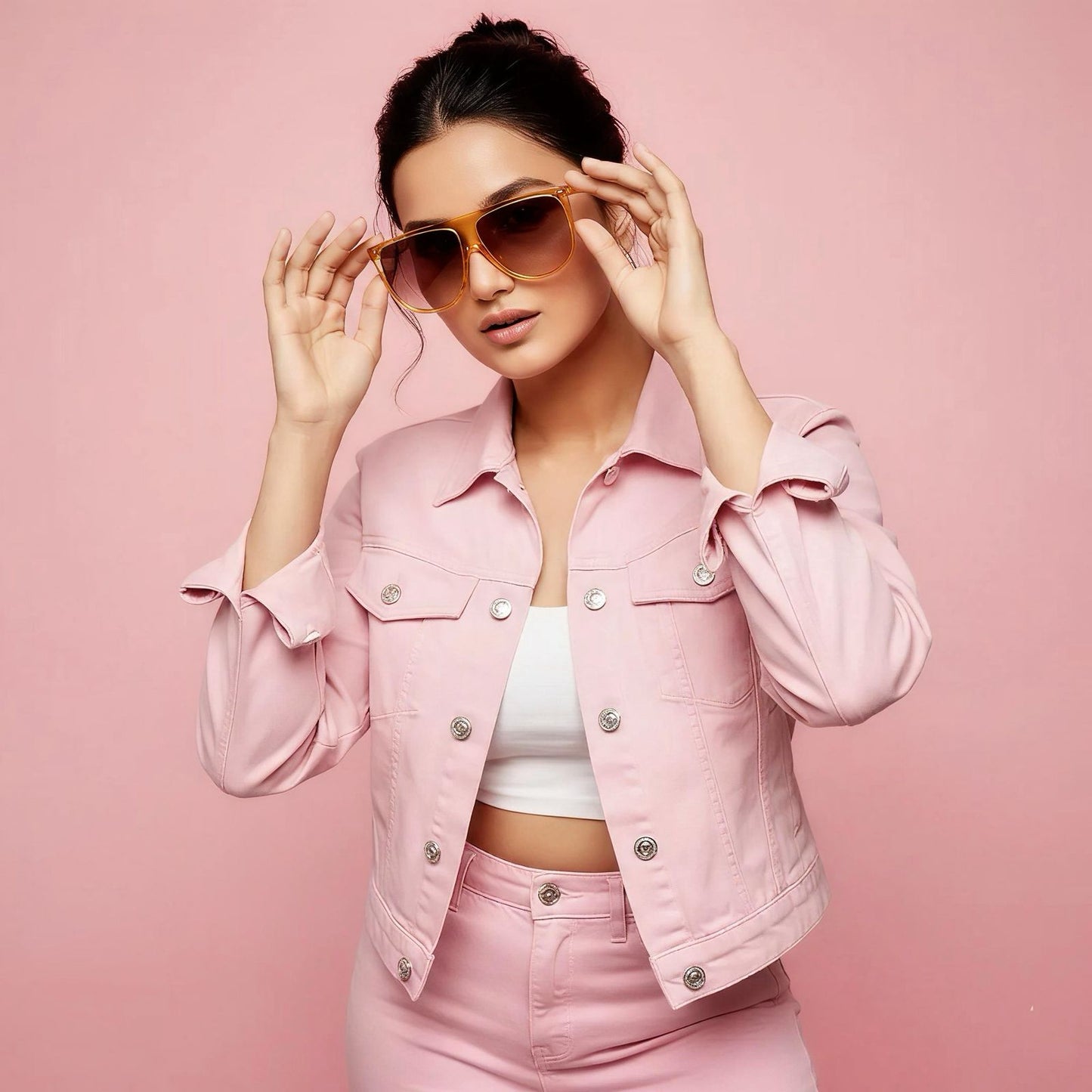 Woman wearing a pink denim outfit with sunglasses on a pink background