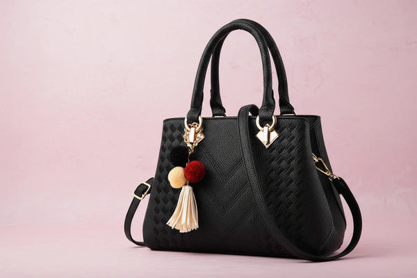 Black handbag with decorative pom-pom and tassel against a blurred architectural background